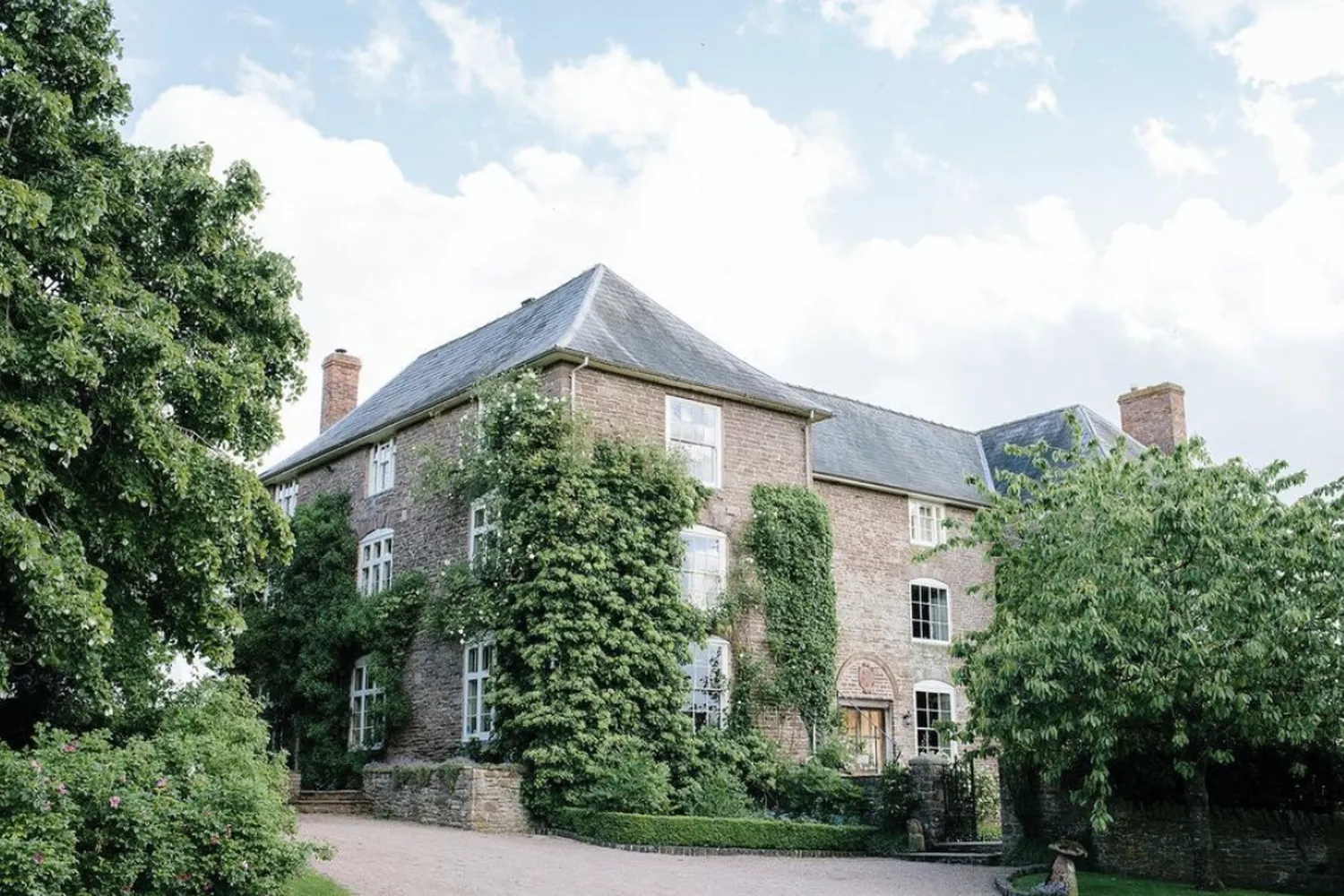 Dewsall Court: an ivy-clad stone house behind mature trees, with a gravel sweep in front.