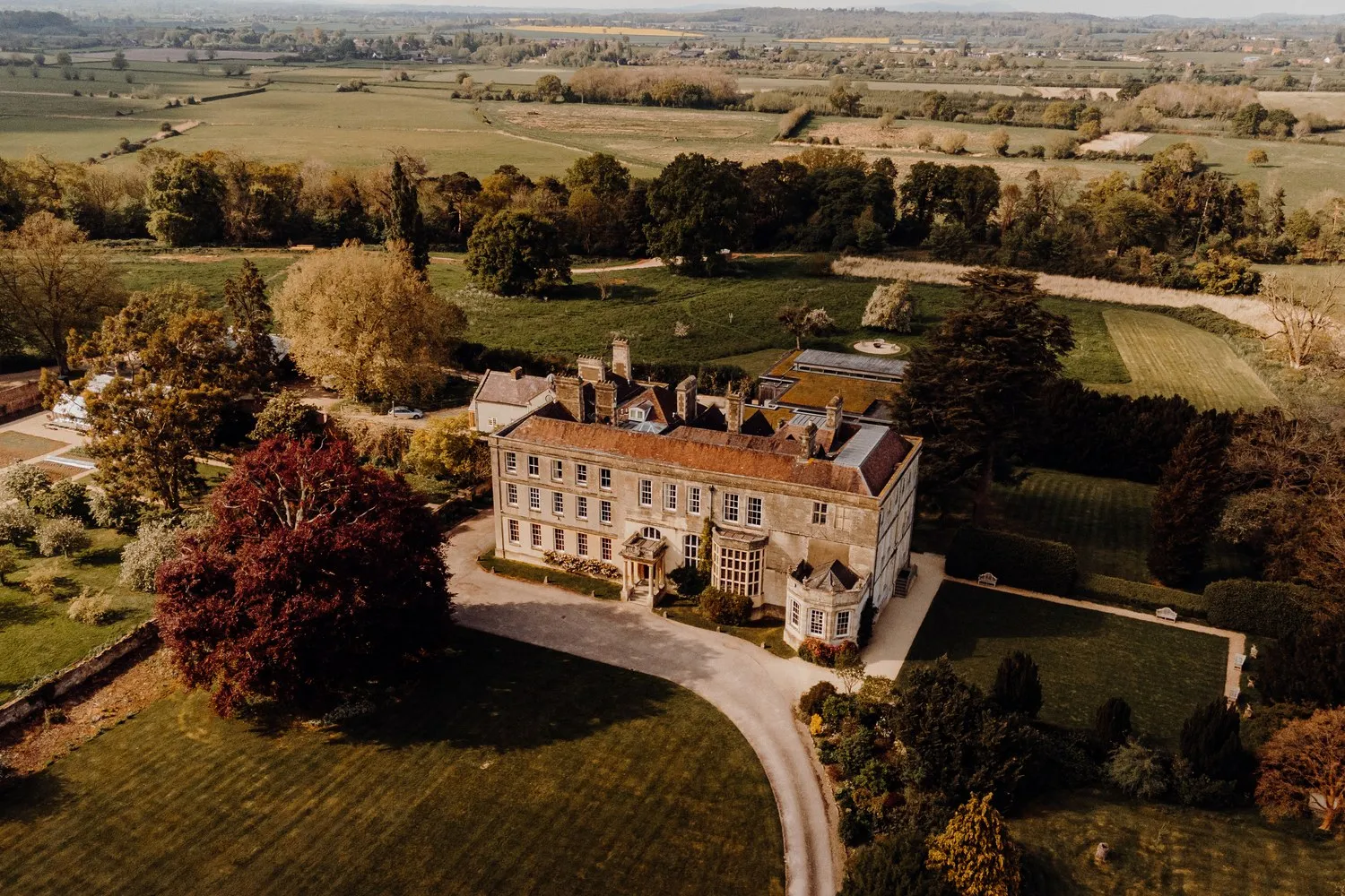 Elmore Court from the air: the Georgian house in its parkland, a copper beech to one side and fields to the horizon.