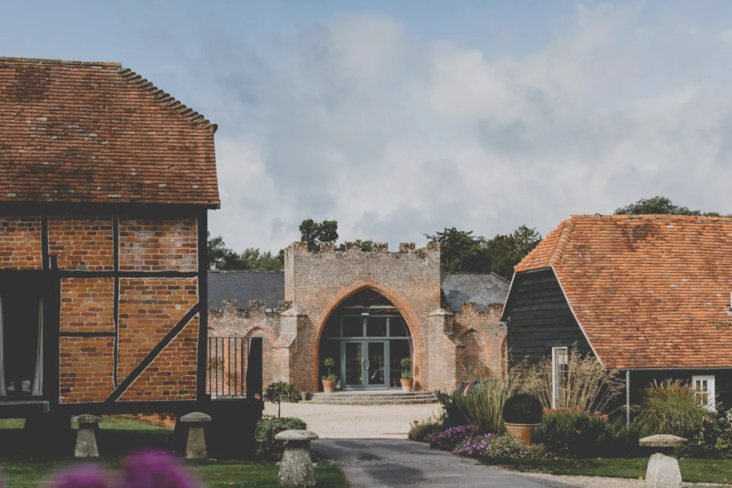Wasing Park: brick-and-timber barns either side of a castellated archway with glazed doors.